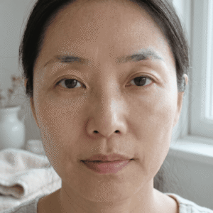 A gentle close-up of a woman's face in soft, natural morning light, noting subtle areas of fatigue and uneven tone before starting her mindful skincare journey