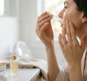 A close-up shot of elegant feminine hands gently pressing a few drops of face serum onto clean glowing skin, soft natural lighting