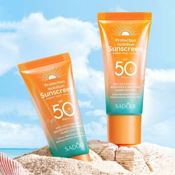 A promotional photograph of two bottles of SADOER Protection Isolation Sunscreen SPF 50 on soft white sand, with a natural shell alongside, set against a clear blue sky with white clouds, in a bright beach scene